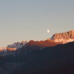 a view of a mountain range with a half moon in the sky